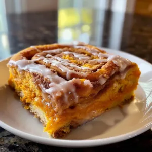 Slice of Pumpkin Cinnamon Roll Cake with cream cheese frosting on a white plate